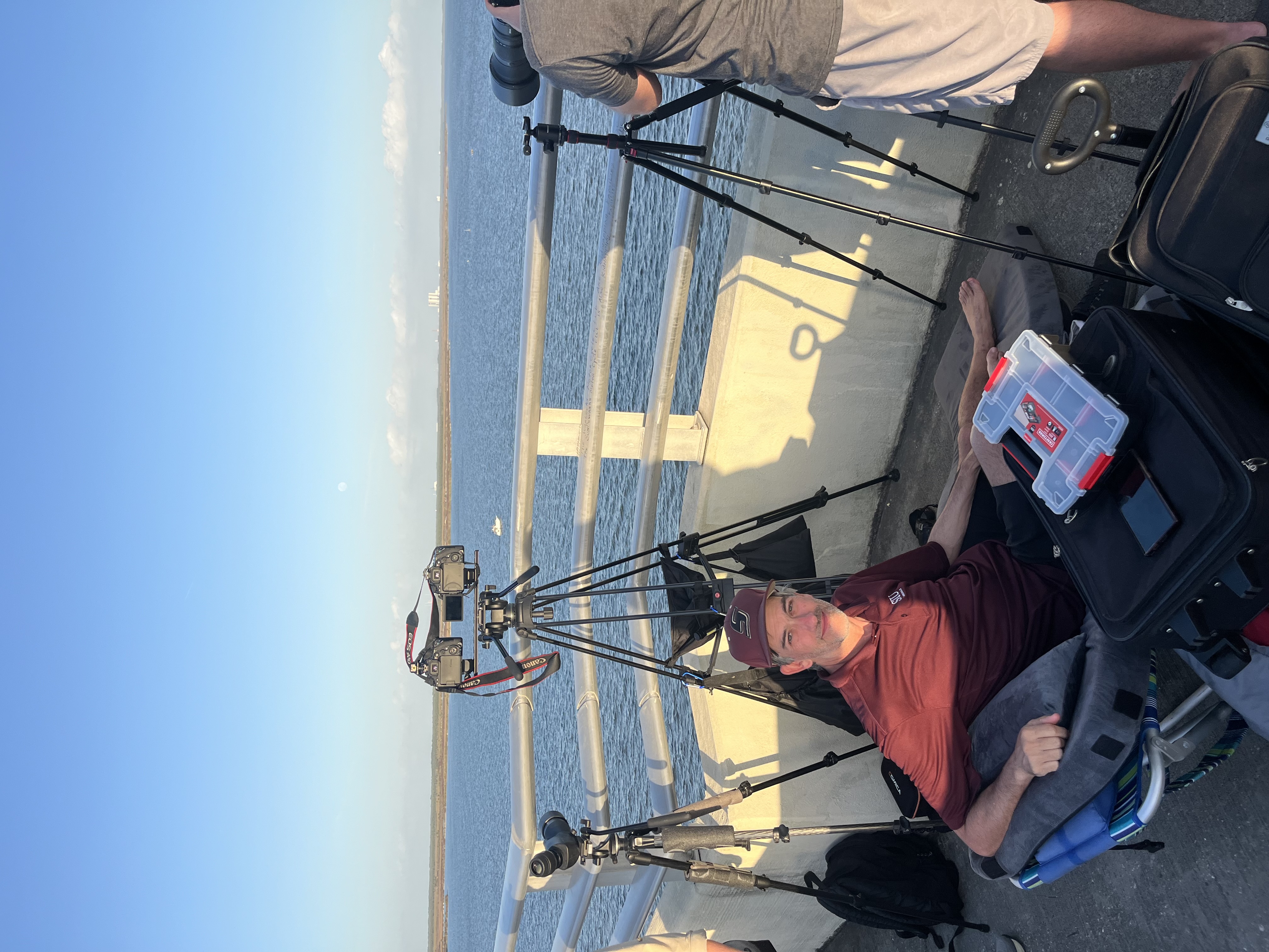 a man sits in a folding chair on a bridge behind cameras on tripods