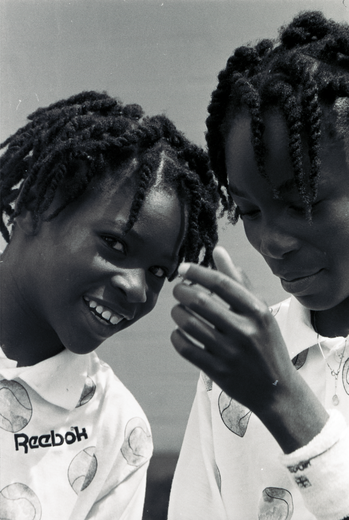 Serena (left) leans in toward her sister Venus (right) and looks at the camera with a smile on her face.